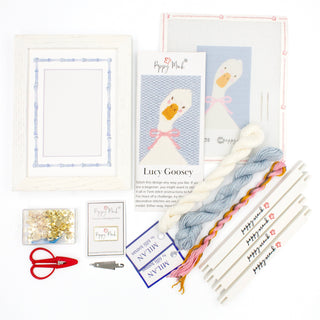 Poppy Monk Lucy Goosey needlepoint canvas shown with kit contents, a white goose with a pink bow on blue